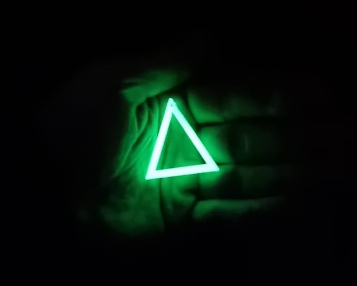 Green to Green Triangle earring In hand glowing in the dark